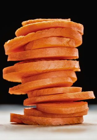 A close-up, high-angle shot of a stack of thinly sliced, vibrant orange carrot rounds on a light surface.の写真素材