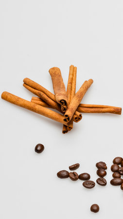 A collection of cinnamon sticks rests on a white surface, accompanied by scattered roasted coffee beans.の写真素材