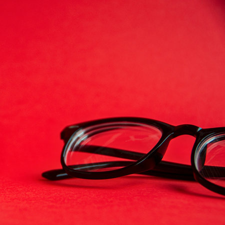 A pair of black-rimmed eyeglasses lies on a solid, bright red surface, creating a bold contrast.の写真素材