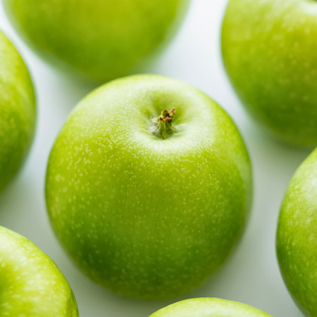 A close-up, overhead view of several vibrant green apples arranged on a clean white background, highlighting their smooth skins and natural beauty.の写真素材