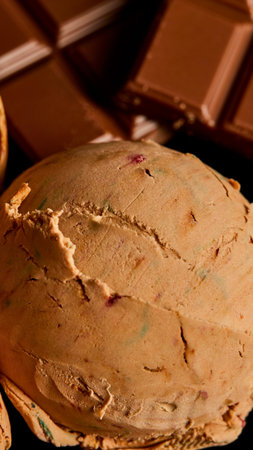 A tempting, golden brown chocolate chip cookie with a cracked surface sits in front of dark chocolate.の写真素材