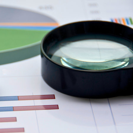 A close-up view of a magnifying glass resting on financial charts and graphs, symbolizing data analysis and research.の写真素材