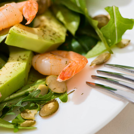 A close-up shot of a vibrant salad featuring succulent shrimp, creamy avocado slices, fresh greens, and scattered seeds, with a fork nearby.の写真素材