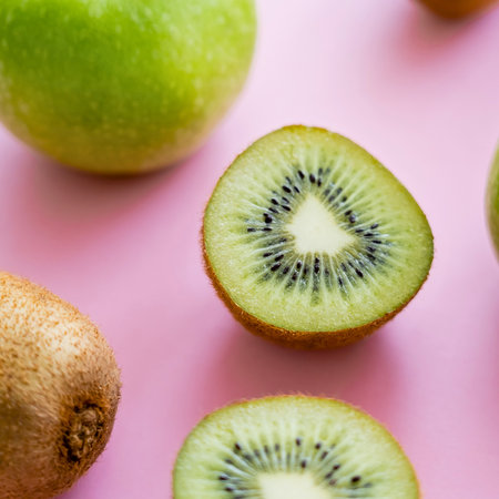 Close-up of vibrant green kiwi fruit, some whole and some sliced in half, artfully arranged on a bright pink surface.の写真素材