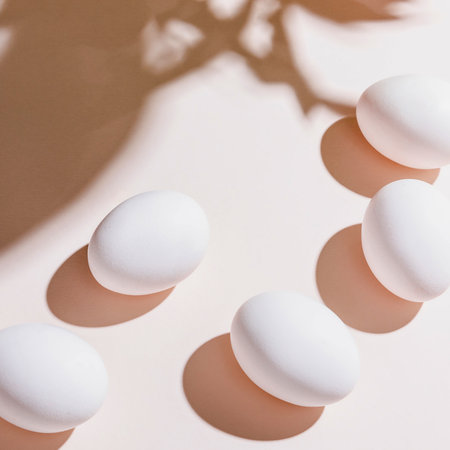 A collection of white and brown eggs appear to float mid-air, casting long, distinct shadows on a soft pink surface.の写真素材