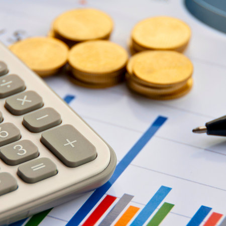 A close-up shot shows a calculator, gold coins, and a pen resting on a financial graph. This image represents financial planning and investment.の写真素材