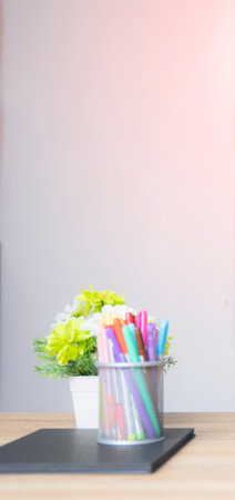 A close-up of a metal cup filled with bright, multicolored drinking straws. A green plant is blurred in the background.の写真素材