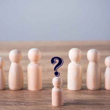 A single wooden peg doll stands out with a question mark, surrounded by other blurred wooden figures, representing doubt or a choice.の写真素材