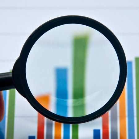 A magnifying glass is held over a vibrant bar graph, highlighting a specific section of financial data and trends.の写真素材
