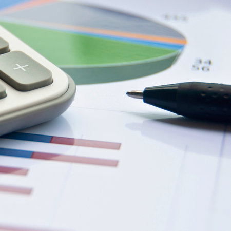 Close up of a calculator, pen, and financial charts including a pie chart and bar graph, suggesting business analysis.の写真素材