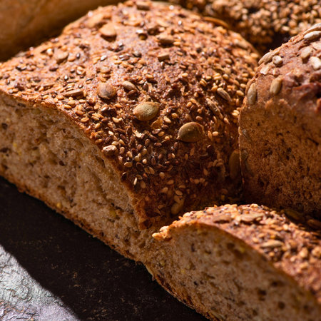 A close-up of a rustic, crusty loaf of whole grain bread covered in a variety of seeds.の写真素材