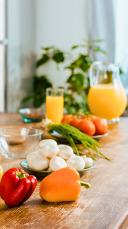 A vibrant arrangement of fresh vegetables and a pitcher of orange juice sits on a rustic wooden table, ready for a healthy meal.の写真素材