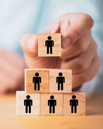 Hands arrange wooden blocks with person icons, forming a pyramid structure representing organizational hierarchy and teamwork.の写真素材