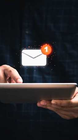 A person's hands hold a tablet device displaying a digital envelope icon with a notification badge indicating one new message.の写真素材