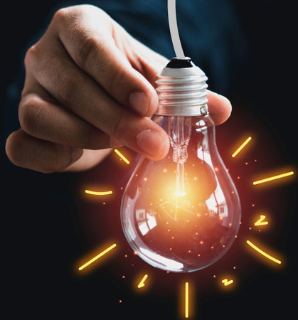A close-up shot of a hand holding a clear incandescent light bulb that is illuminated with a bright,...