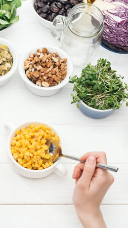 A hand uses a spoon to scoop bright orange food from a white bowl, surrounded by other bowls of ingredients.の写真素材