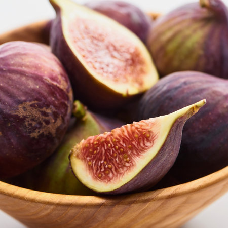 A close-up shot of a wooden bowl filled with ripe purple figs, some whole and some cut in half revealing their juicy interior.の写真素材