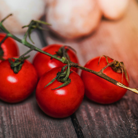 Close-up of ripe red cherry tomatoes still attached to their vines, resting on a textured wooden background.の写真素材