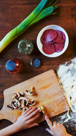 A close-up overhead view of pizza ingredients including sliced mushrooms, salami, leeks, and spices on a wooden surface.の写真素材