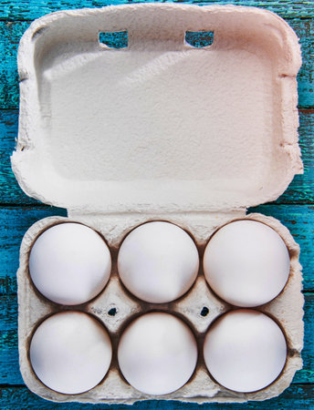 An overhead view of a carton containing six fresh white eggs, resting on a vibrant blue wooden background.の写真素材