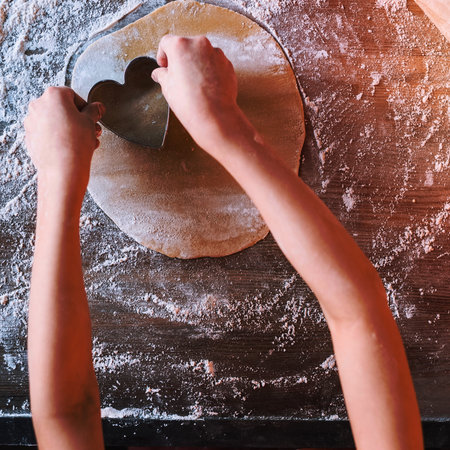 A person's hands are shown from above, using a decorative cookie cutter to shape dough on a textured surface.の写真素材