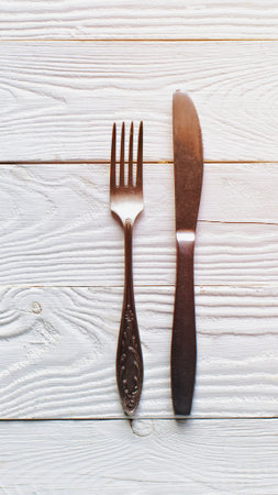 A fork and knife are laid out on a rustic white wooden surface, ready for a meal. The lighting is bright and airy.の写真素材