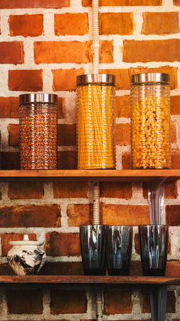 Three glass jars filled with different types of pasta sit on a wooden shelf, with bowls below, against a brick wall.の写真素材