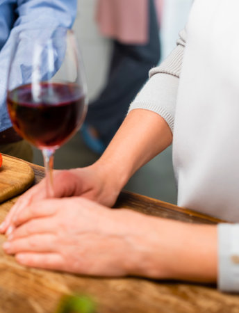 A person's hands are reaching towards a table with a glass of red wine and food, suggesting a meal or gathering.の写真素材