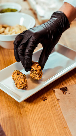 A gloved hand carefully places a small, golden-brown pastry onto a rectangular white serving dish on...