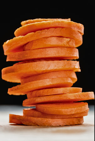 A close-up, high-angle shot of a stack of thinly sliced, bright orange carrot rounds against a dark background.の写真素材