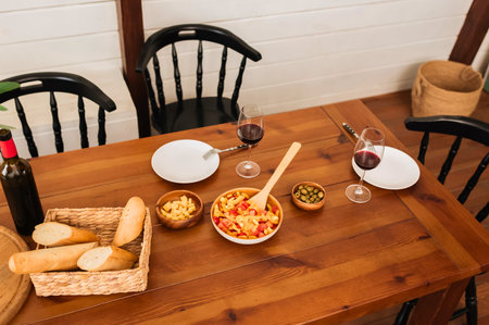 A rustic wooden table is set with plates, bowls of food, bread, and a bottle of wine, ready for a gathering.の写真素材