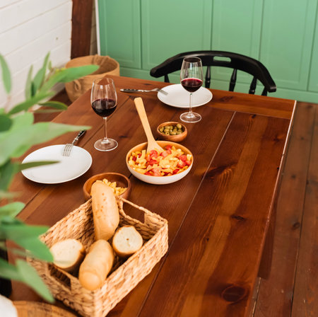 A warm, inviting scene of a wooden table laden with fresh bread, a colorful salad, and wine glasses, ready for a meal.の写真素材