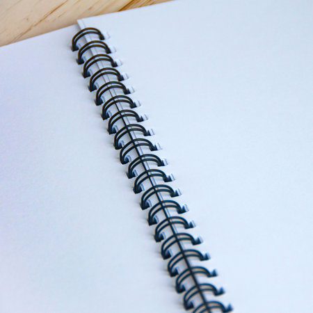 A detailed view of the black spiral binding on a white notebook, with a hint of a tan cover in the background.の写真素材