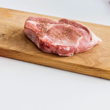 A single, raw pork chop with bone is presented on a rustic wooden cutting board, ready for preparation.の写真素材