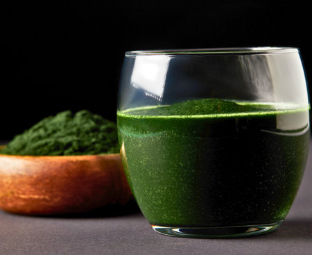 A refreshing green smoothie in a glass next to a bowl of bright green spirulina powder, showcasing a healthy lifestyle.の写真素材