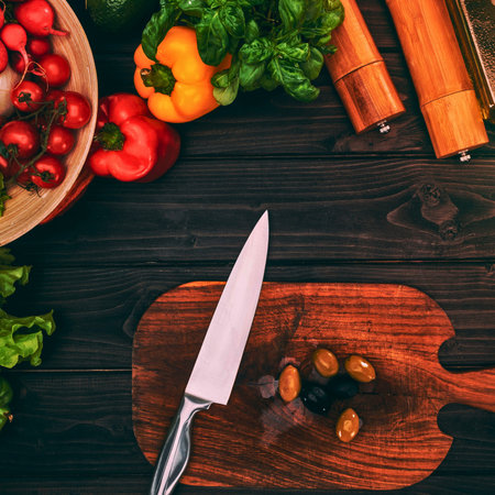 A vibrant overhead shot of fresh produce including carrots, peppers, and tomatoes, with a knife on a rustic wooden cutting board.の写真素材