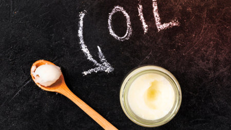 A wooden spoon holds a scoop of solid coconut oil next to a jar of the same oil. Chalk spells out 'oil' on a dark background.の写真素材