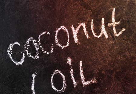 The words coconut oil are written in white chalk on a dark, textured background. The lettering is...