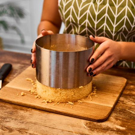 A person's hands hold a metal cake ring around a layered dessert on a cutting board, preparing it for assembly or serving.の写真素材