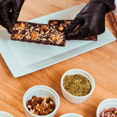 Hands in black gloves hold two delicious homemade granola bars on a white plate, with small bowls of nuts and seeds in the foreground.の写真素材