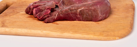 A close-up shot of a raw, deep red beef steak resting on a light-colored wooden cutting board, prepared for meal preparation.の写真素材