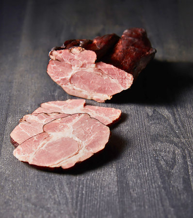 Two slices of smoked pork shoulder are displayed on a dark, textured surface, showcasing the meat's marbled texture and pink hue.の写真素材
