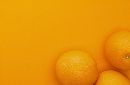 A close-up, top-down view of several ripe oranges arranged on a solid, bright orange surface with a soft focus.の写真素材