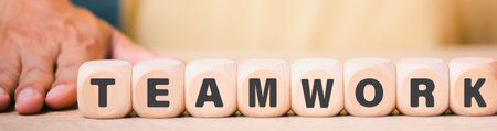 A close-up of wooden blocks spelling out the word TEAMWORK, with a person's hand subtly visible on the left.の写真素材