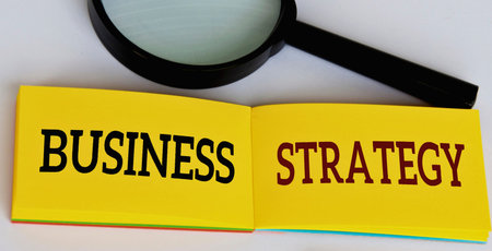 A magnifying glass hovers over an open book with the words Business Strategy printed in bold...