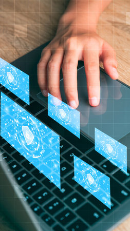 A hand interacts with a glowing blue holographic interface projected above a laptop keyboard,...