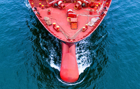 An overhead perspective of a large red cargo ship's bow as it navigates through the deep blue sea,...
