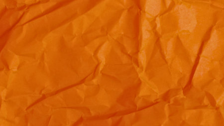 A close-up, abstract view of wrinkled orange fabric, showcasing its texture, folds, and the play of light and shadow.の写真素材