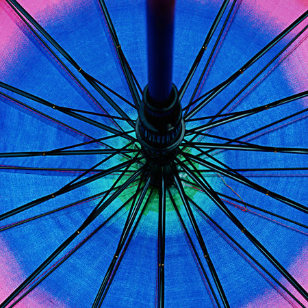 Close-up view of the underside of an open umbrella, showcasing its intricate metal ribs against a vibrant, colorful fabric background.の写真素材