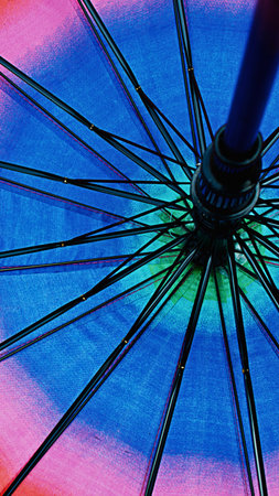Close-up view of the inside of a colorful umbrella, showcasing its radial metal spokes against a backdrop of vibrant rainbow fabric.の写真素材
